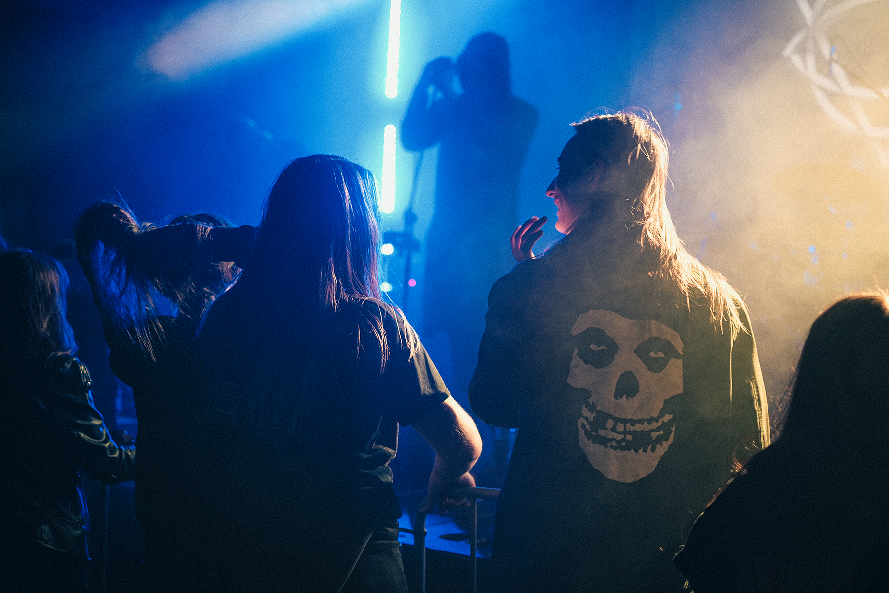 Publiczność na koncercie rockowym i metalowym w klubie, sylwetki fanów pod sceną w kolorowym oświetleniu, atmosfera live show i muzyki na żywo.