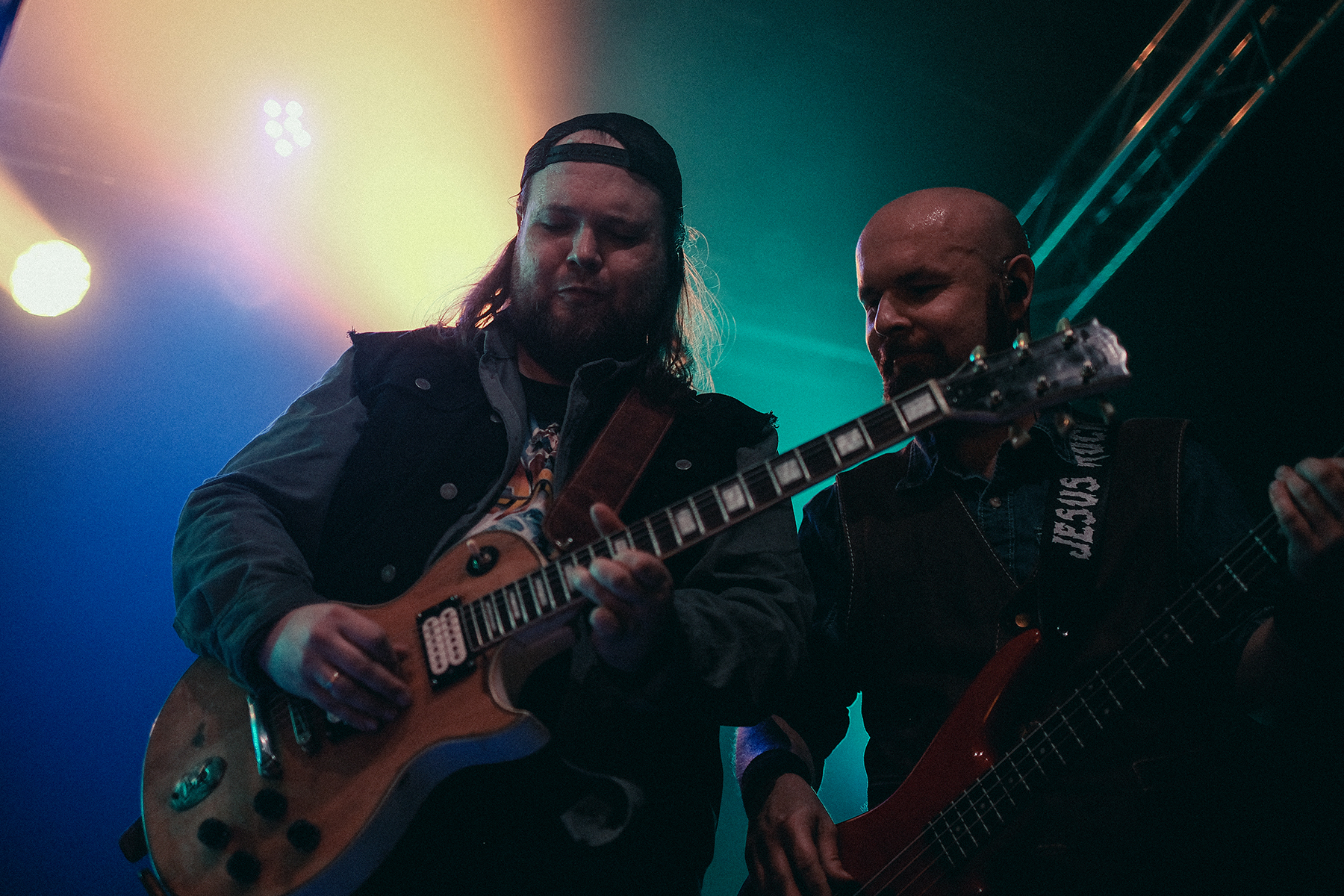 Dwóch muzyków wrocławskiego zespołu Mama Morphine podczas koncertu na Wajbzzfest! 2025 gra wspólnie na scenie pod intensywnym niebiesko-zielonym oświetleniem. Gitarzysta i basista stoją blisko siebie, skupieni na występie, a zdjęcie oddaje energię i koncertową atmosferę rockowego grania na żywo.