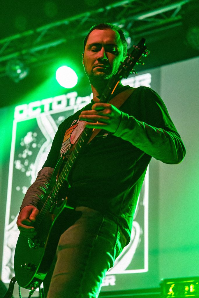 Wojtek, gitarzysta zespołu Octotanker, skupiony podczas koncertu wśród zielonych świateł i scenicznego dymu.