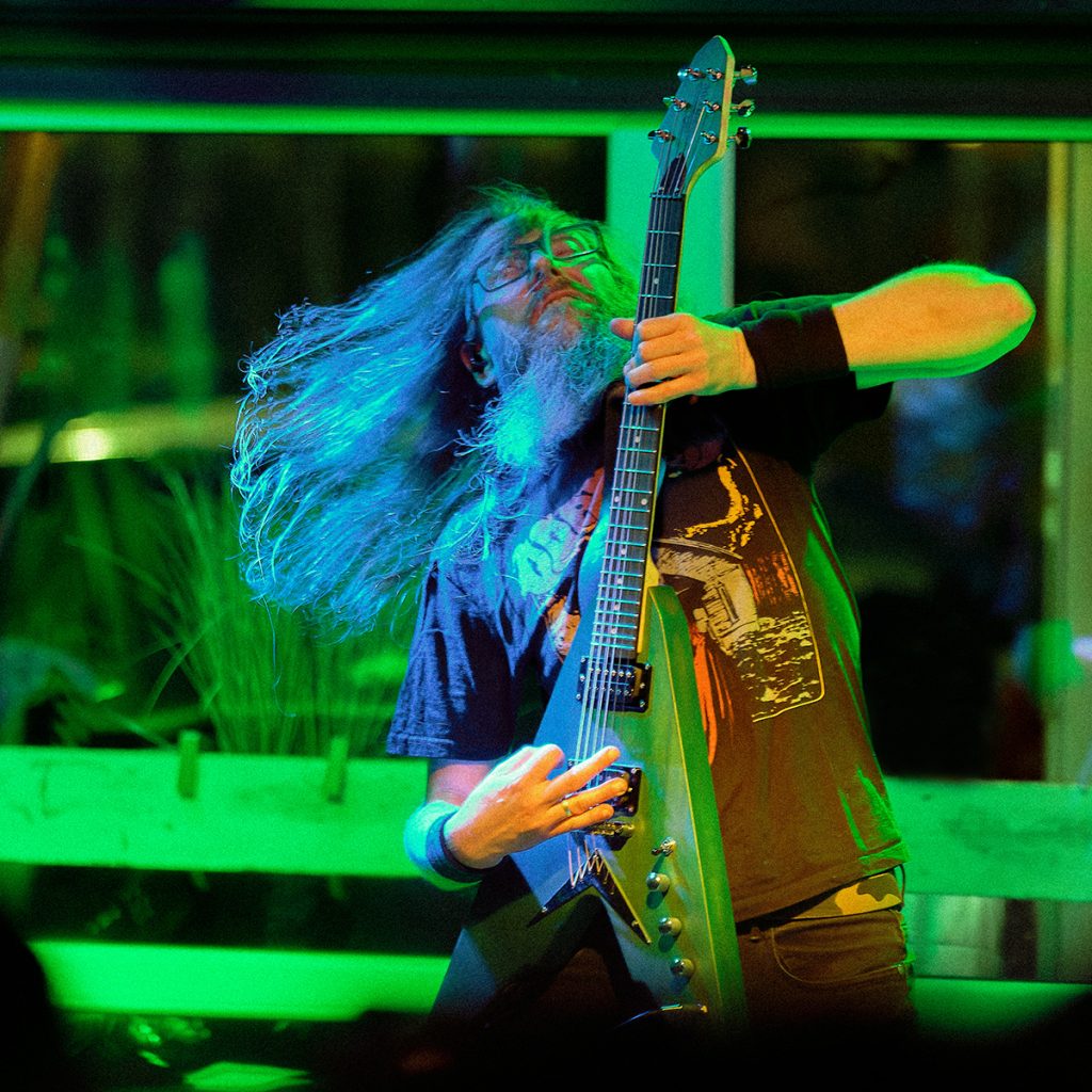 Piotrek, gitarzysta wrocławskiego GMOH, podczas koncertu w klubie Alive pod nasypem we Wrocławiu. Dynamiczna poza i charakterystyczna gitara elektryczna oddają energię występu, w którym ciężkie riffy przeplatają się z melodyjnymi partiami budującymi niepowtarzalny klimat blackened death metalu.