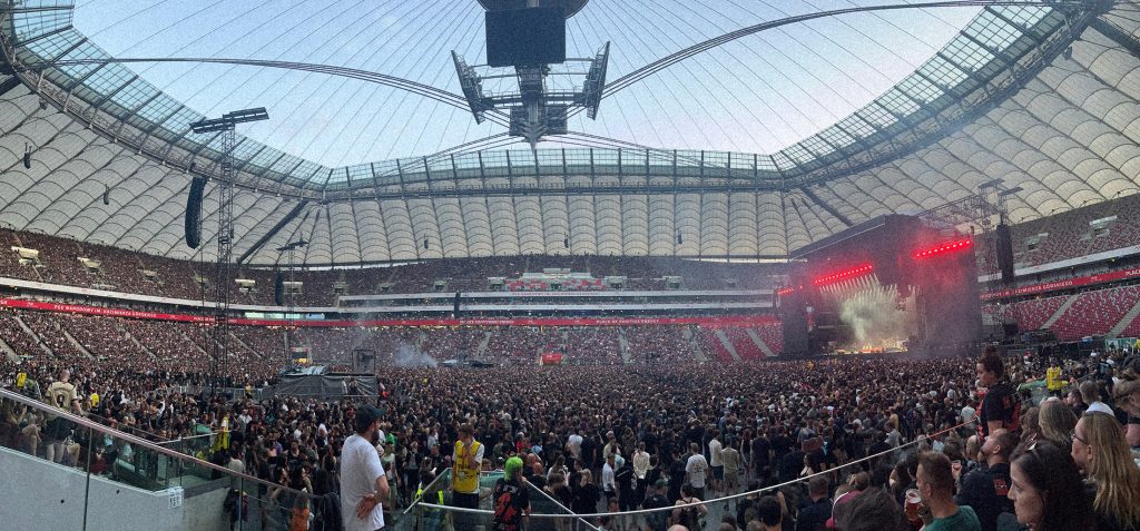 Tysiące fanów zgromadzonych na PGE Narodowym w Warszawie podczas koncertu System of a Down i Queens of the Stone Age 18 lipca 2026 roku. Panorama stadionu ukazuje ogromną scenę oraz wypełnione po brzegi trybuny i płytę.