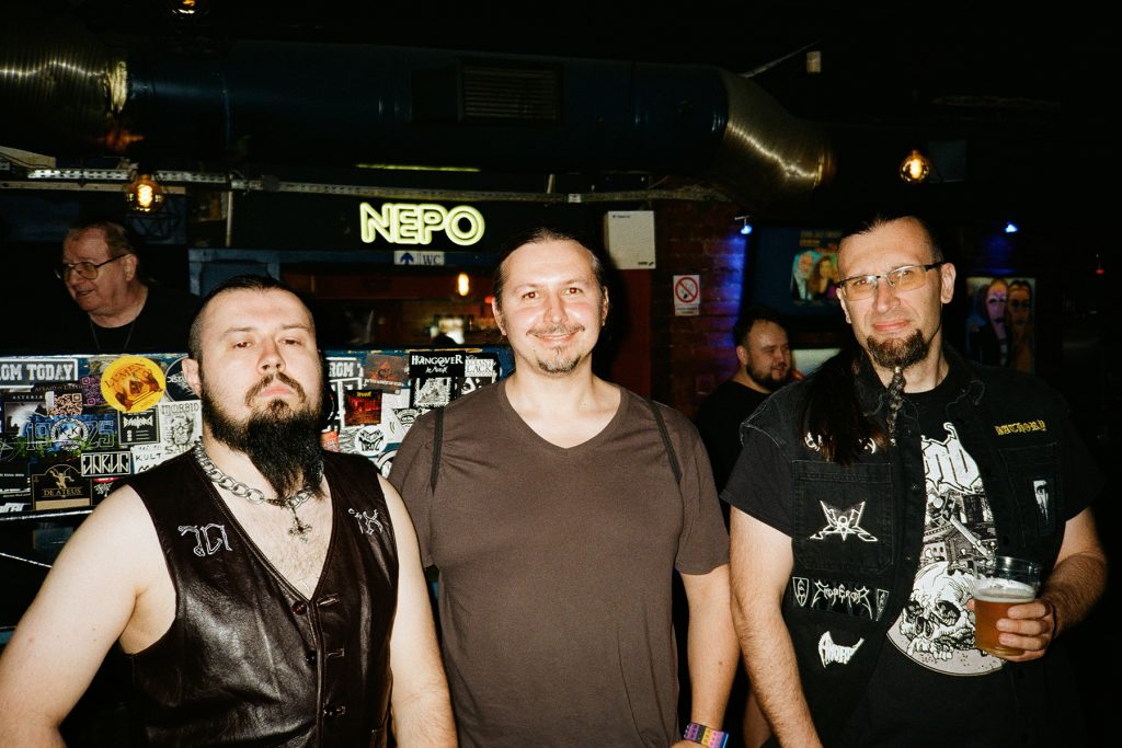 Marcin, przyjaciel zespołu i Filip, członkowie Vae Solis, pozujący wspólnie przed koncertem w klubie Liverpool podczas wydarzenia „Brudna Odra”. W tle widoczny bar z charakterystycznym neonem NEPO.