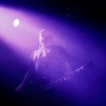 Kai, gitarzysta i wokalista NOOMN, podczas koncertu we Wrocławiu, oświetlony intensywnym fioletowym światłem i spowity sceniczną mgłą.